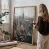Large framed print of the NYC skyline featuring the Empire State Building, leaning against a wall beside a woman in a cozy home setting.