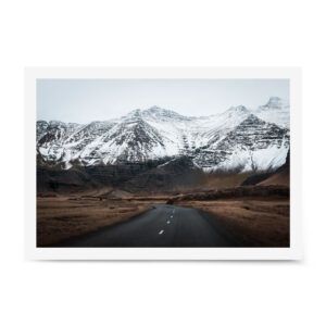 Snow-dusted mountains rise above an empty road leading through a remote Icelandic valley.