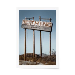 Photograph of a sun-bleached roadside “Nothing” sign standing tall in the Arizona desert under a clear blue sky with dry brush and mountains.